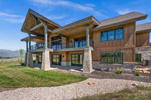 Rear view of house featuring a balcony, stone siding, a patio, and a lawn