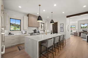Kitchen featuring tasteful backsplash, an island with sink, a sink, light stone counters, and a breakfast bar