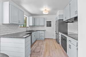 Kitchen featuring black oven, a sink, under cabinet range hood, light wood-style floors, and tasteful backsplash