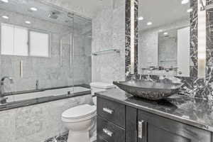 Bathroom featuring toilet, a combined bath / shower with rainfall shower, vanity, recessed lighting, and tile walls