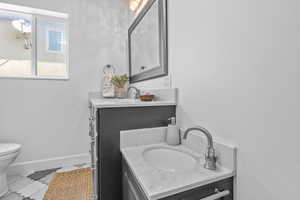 Bathroom featuring vanity, toilet, marble finish flooring, and baseboards