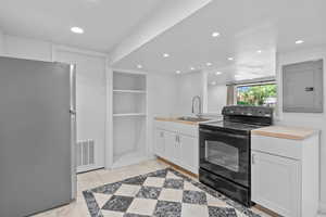 Kitchen featuring freestanding refrigerator, black electric range oven, electric panel, a sink, and recessed lighting
