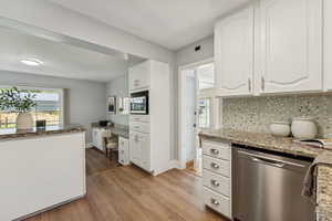 Kitchen featuring appliances with stainless steel finishes, white cabinetry, light stone countertops, dark wood-type flooring, and backsplash