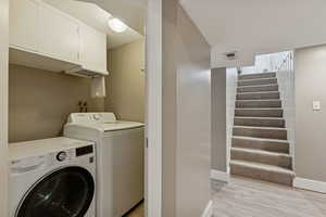 Washroom with light wood-type flooring, independent washer and dryer, and cabinet space