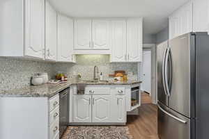Kitchen with appliances with stainless steel finishes, light stone counters, backsplash, and white cabinets