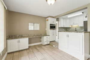Kitchen featuring white cabinets, stainless steel microwave, baseboards, decorative backsplash, and a sink