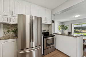 Kitchen featuring appliances with stainless steel finishes, dark stone counters, decorative backsplash, white cabinets, and light wood finished floors