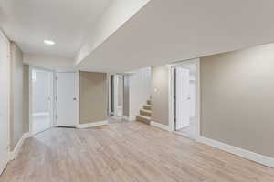 Finished basement with light wood-style flooring, stairs, and recessed lighting