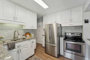 Kitchen featuring appliances with stainless steel finishes, light stone countertops, white cabinetry, and tasteful backsplash