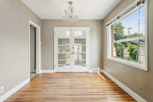 Unfurnished dining area featuring french doors, a chandelier, light wood finished floors, and baseboards