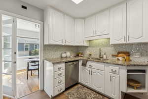 Kitchen featuring dark stone counters, white cabinets, decorative backsplash, dark wood finished floors, and dishwasher