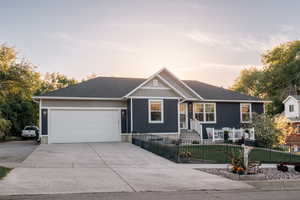 Ranch-style house featuring an attached garage, concrete driveway, a fenced front yard, and roof with shingles