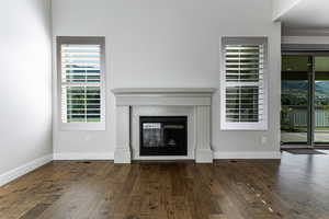 Unfurnished living room featuring hardwood / wood-style flooring, a glass covered fireplace, and baseboards