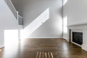 Unfurnished living room featuring a high ceiling, a glass covered fireplace, wood finished floors, and baseboards