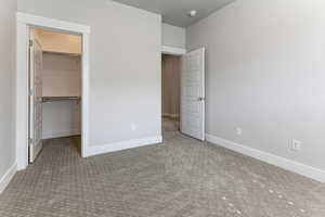 Unfurnished bedroom with carpet floors, baseboards, a walk in closet, and a closet