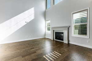 Unfurnished living room featuring a glass covered fireplace, hardwood / wood-style floors, baseboards, and a towering ceiling