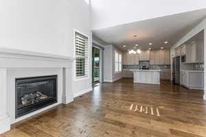 Unfurnished living room with a chandelier, a glass covered fireplace, dark wood-style flooring, recessed lighting, and baseboards