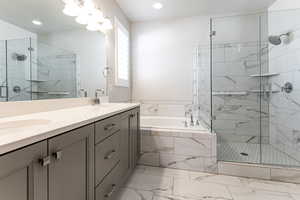 Bathroom featuring a bath, double vanity, a stall shower, marble look tiles, and recessed lighting