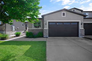 View of front of home featuring brick siding, an attached garage, concrete driveway, a front yard, and stucco siding