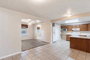 Kitchen featuring white appliances, arched walkways, light countertops, under cabinet range hood, and baseboards