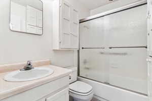 Bathroom with vanity, bath / shower combo with glass door, and toilet