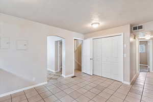 Unfurnished bedroom with arched walkways, light tile patterned floors, a closet, a textured ceiling, and baseboards