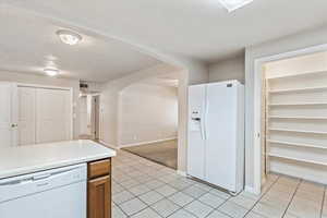 Kitchen with white appliances, light tile patterned floors, arched walkways, light countertops, and baseboards