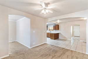 Kitchen featuring light carpet, light tile patterned floors, a ceiling fan, and arched walkways