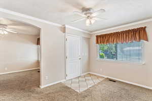 Unfurnished bedroom with arched walkways, baseboards, a textured ceiling, light carpet, and a ceiling fan