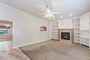 Unfurnished living room with a ceiling fan, a fireplace, lofted ceiling, baseboards, and light carpet