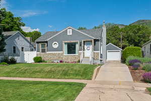 Bungalow-style home featuring stucco siding, stone siding, a detached garage, an outdoor structure, and concrete driveway