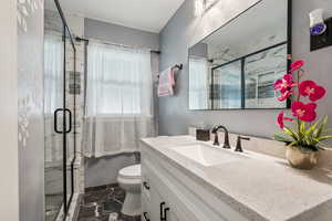 Bathroom featuring marble look tiles, vanity, a marble finish shower, and toilet