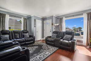 Living area with dark wood-type flooring, crown molding, and baseboards