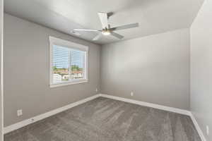 Empty room featuring dark carpet, a ceiling fan, and baseboards