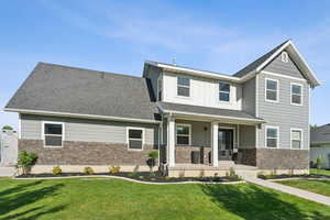 Craftsman-style house featuring stone siding, a porch, a front yard, and board and batten siding
