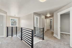 Hall with an upstairs landing, carpet flooring, a chandelier, and baseboards