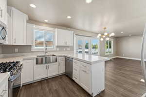 Kitchen with appliances with stainless steel finishes, a sink, a peninsula, dark wood-style flooring, and white cabinetry