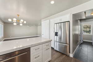 Kitchen with appliances with stainless steel finishes, light stone counters, white cabinets, baseboards, and a chandelier