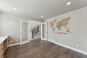 Empty room featuring french doors, dark wood finished floors, stairway, baseboards, and recessed lighting