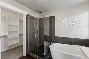 Full bathroom with a stall shower, a walk in closet, a freestanding tub, and tile walls