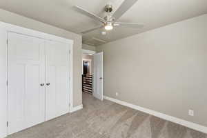 Unfurnished bedroom featuring carpet flooring, baseboards, a closet, attic access, and a ceiling fan