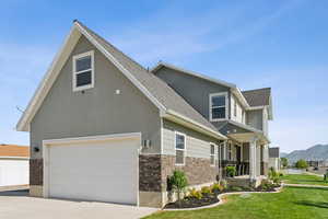 View of front facade with stone siding, a garage, concrete driveway, a front lawn, and a porch