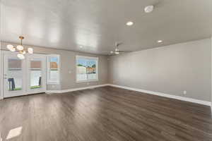 Unfurnished living room with baseboards, dark wood-style flooring, ceiling fan, a chandelier, and recessed lighting