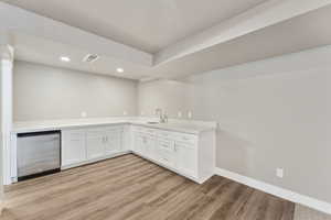 Indoor bar with stainless steel dishwasher, light wood-type flooring, baseboards, and recessed lighting