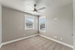 Carpeted spare room featuring ceiling fan and baseboards