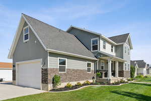 View of front facade featuring stone siding, a garage, a shingled roof, a front lawn, and driveway