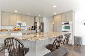 Kitchen with white appliances, recessed lighting, arched walkways, a breakfast bar, and dark wood-style flooring