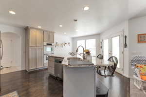 Kitchen featuring stainless steel dishwasher, white double oven, a sink, a breakfast bar, and dark wood-style flooring