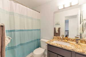 Bathroom featuring toilet, vanity, and curtained shower