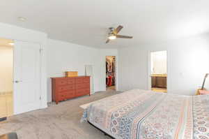 Carpeted bedroom featuring a walk in closet, a closet, ceiling fan, ensuite bath, and baseboards